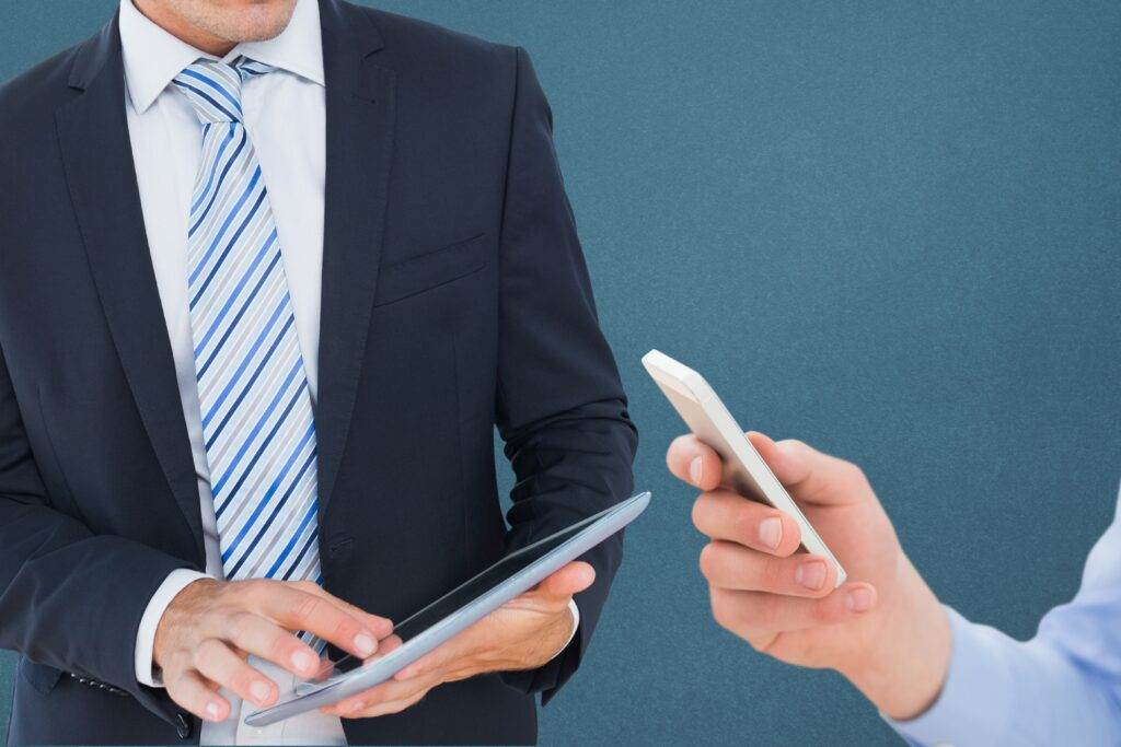 Businessman using tablet, another person holding smartphone.