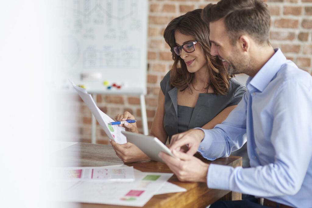 Two business colleagues review financial documents and a tablet, discussing an Australian Financial Services Licence application.