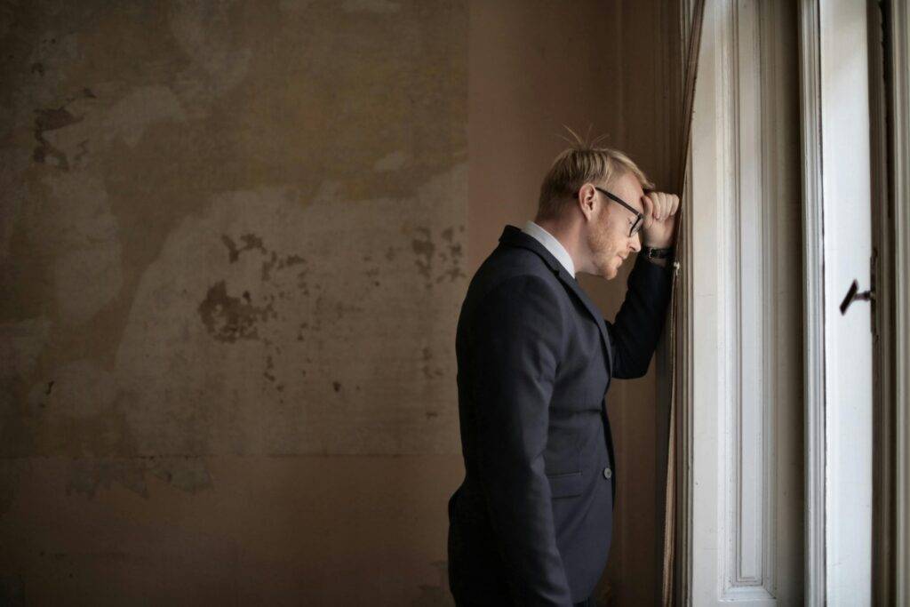 Man in suit looking out a window with a thoughtful expression