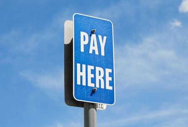 Blue "Pay Here" sign against a bright blue sky.