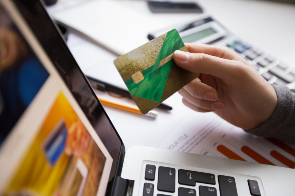 Hand holding a credit card near a laptop, calculator, and documents. Online payment.