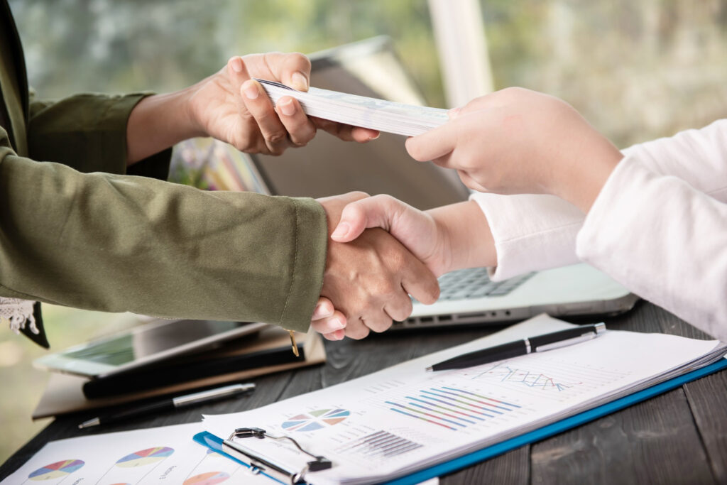 Handshake with money exchange over financial charts, representing stablecoin regulations in Australia.