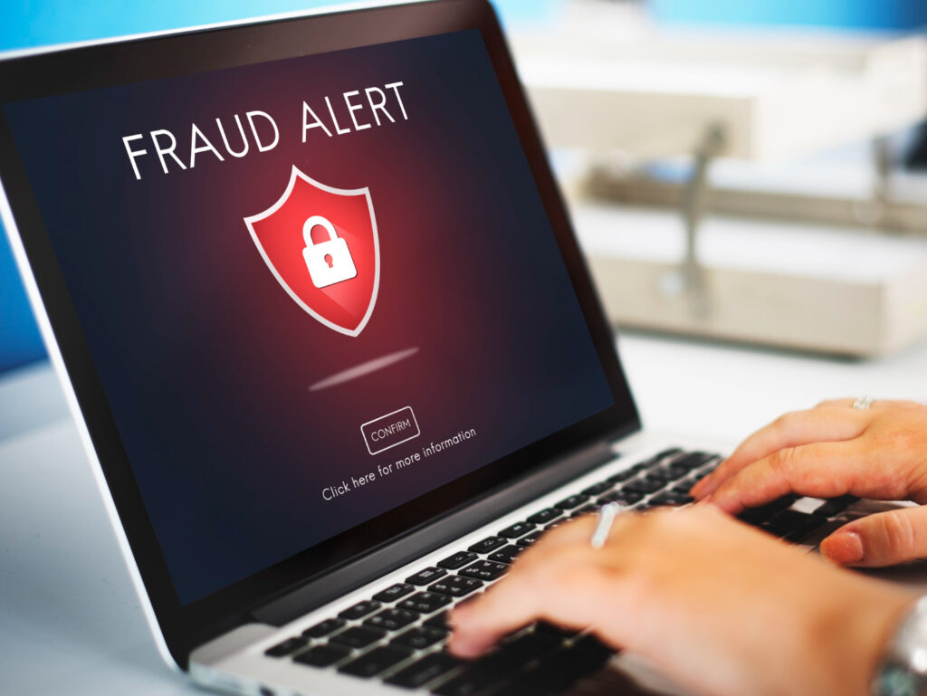 Laptop screen displays "FRAUD ALERT" with a shield icon, representing share sale fraud.
